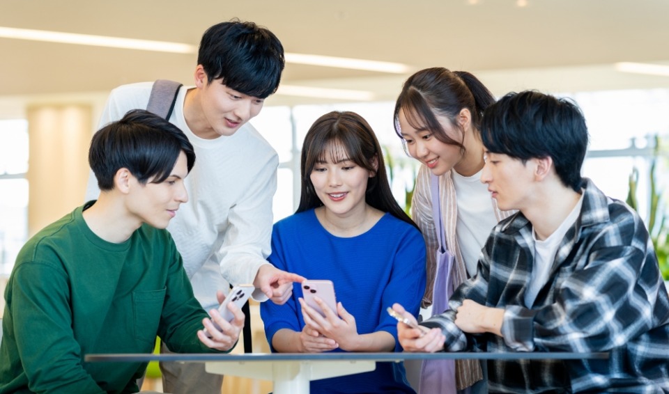 男女の学生がスマホを囲んでいる写真